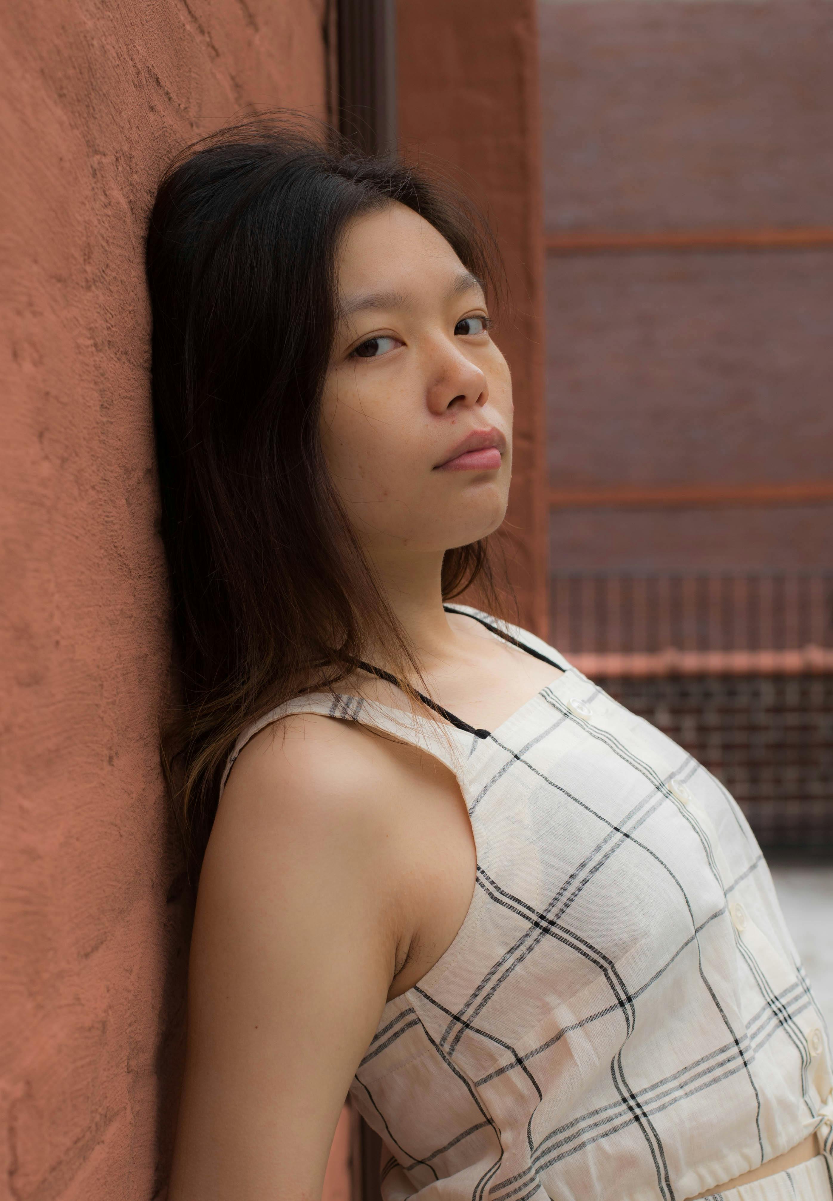 A fashionable woman poses confidently against a rustic brick wall in an outdoor setting.