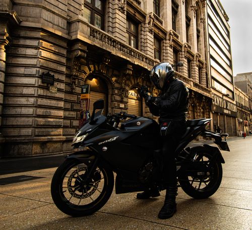 Free Motorcyclist adjusting helmet in front of historic city building at day. Stock Photo