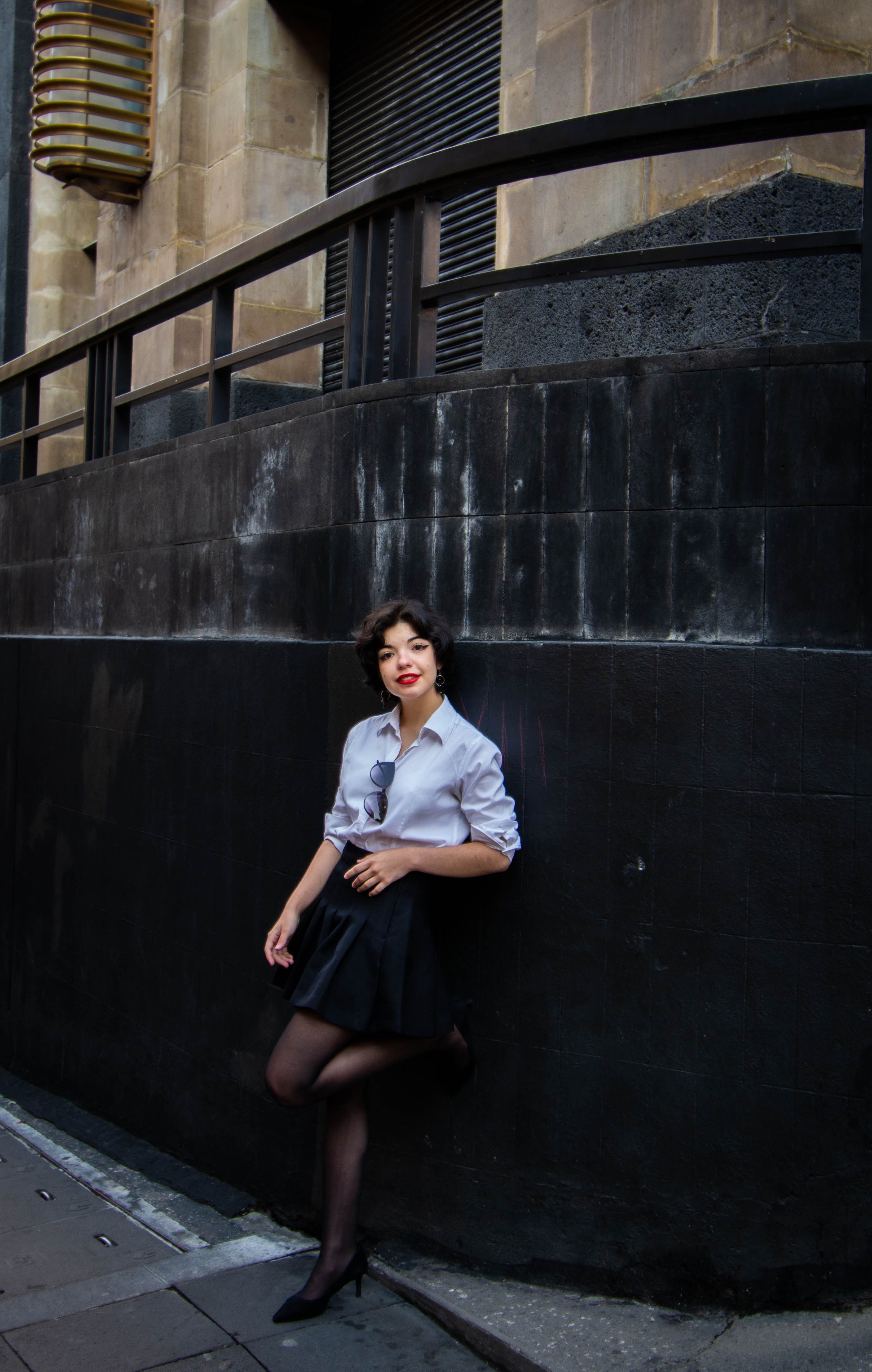 A Woman in White Dress Shirt and Black Skirt Leaning on Black Concrete ...