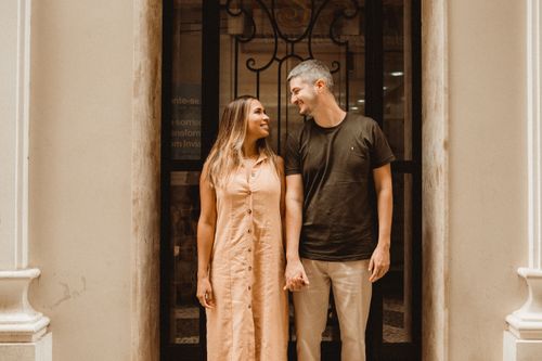 Free A joyful couple standing outside holding hands, smiling and looking at each other. Stock Photo