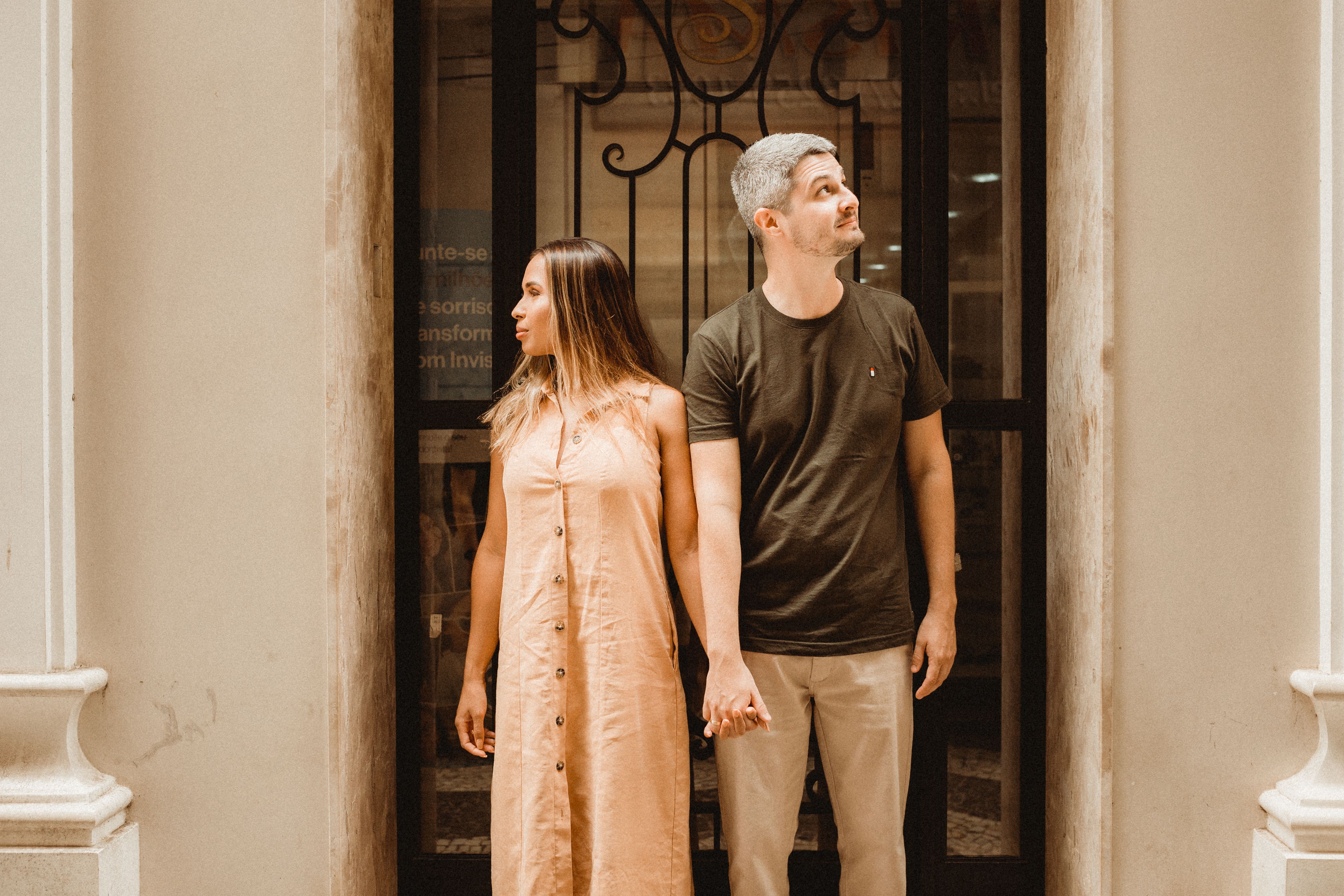 couple in coordinated neutral tones with warm earth colors standing on an urban rooftop overlooking a city skyline at dusk, relaxed and laughing together, engagement session editorial look