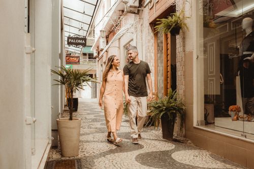 Free A joyful couple walks hand-in-hand through a charming city alley lined with shops and greenery. Stock Photo