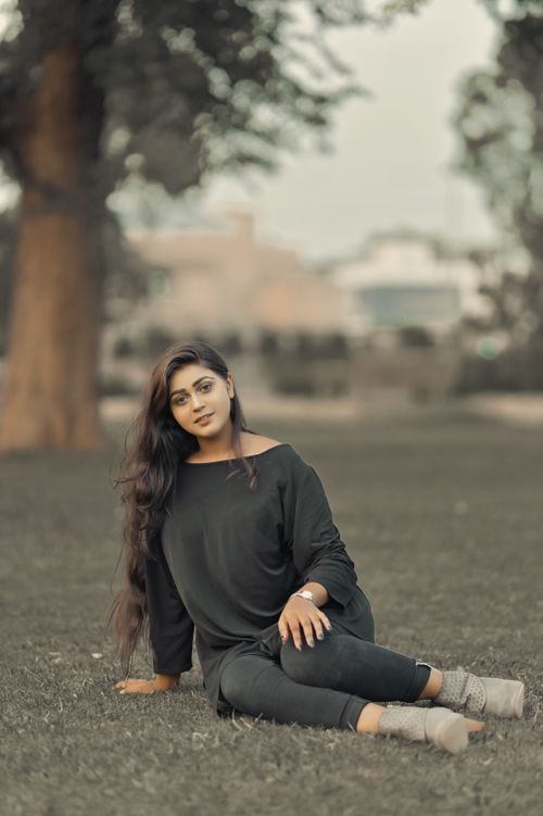 Free A fashionable woman sitting on grass in a park, showcasing modern style with long hair and a smile. Stock Photo