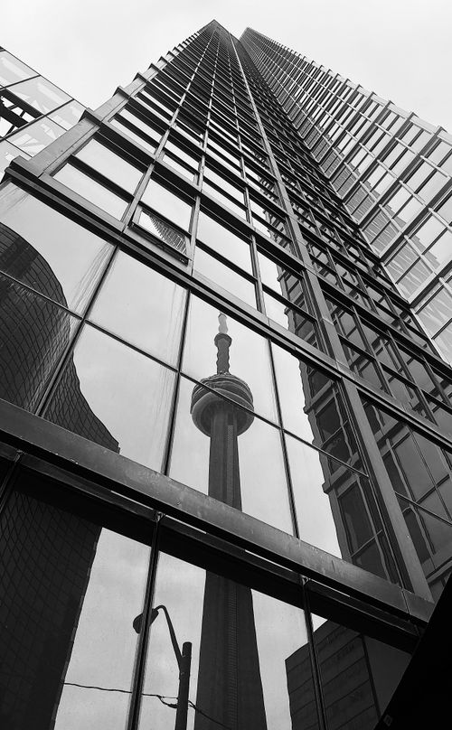 Free Black and white shot of a famous tower reflected on a modern building's glass facade. Stock Photo
