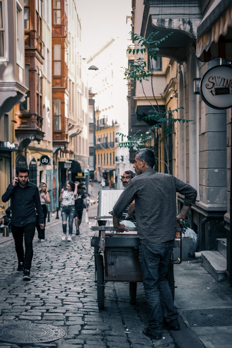 A Man Pushing A Cart On The Street