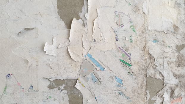 Close-up of peeling paper layers on textured wall, revealing vibrant colors underneath.
