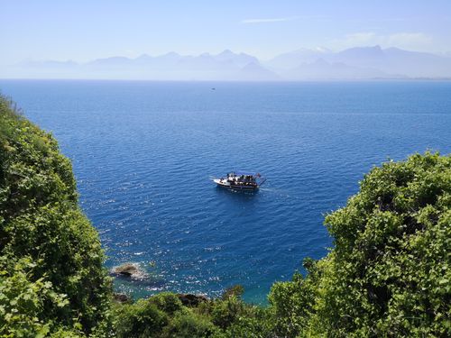 Free A picturesque boat sailing in the blue waters of Antalya, Turkey, with lush greenery and mountains. Stock Photo