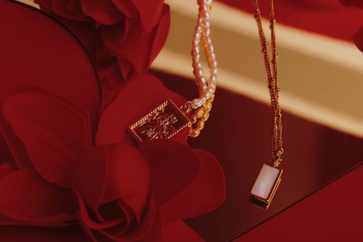 Close-up of gold and pearl necklaces on red floral background, elegant design.