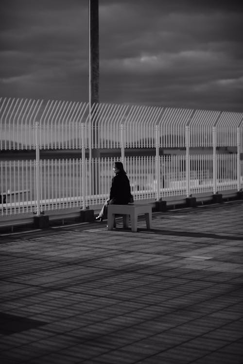 Free A Grayscale Photo of a Woman Sitting on the Bench Stock Photo