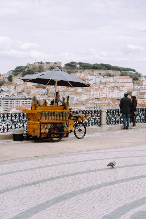 Fruit Stand under an Umbrella on a Bridge with Tourist Couple, with a View on a City in Lisbon, Portugal