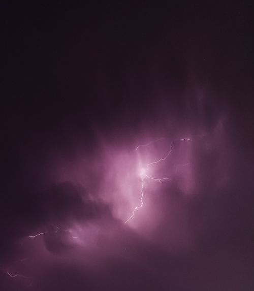 Free Purple lightning bolts illuminate a moody night sky creating a dramatic scene. Stock Photo