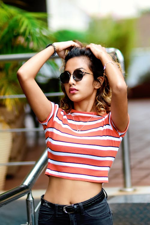 Free A Woman in Striped Shirt Wearing Sunglasses with Her Hands on Her Head Stock Photo