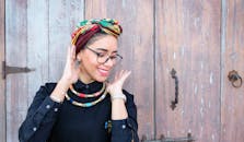 一位时尚女性头戴头巾、颈戴项链，在质朴的木门前微笑