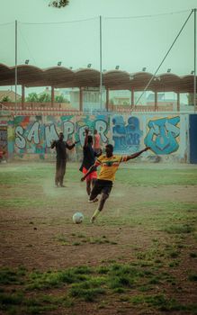 Group of young men playing football on a dusty field with colorful graffiti backdrop.