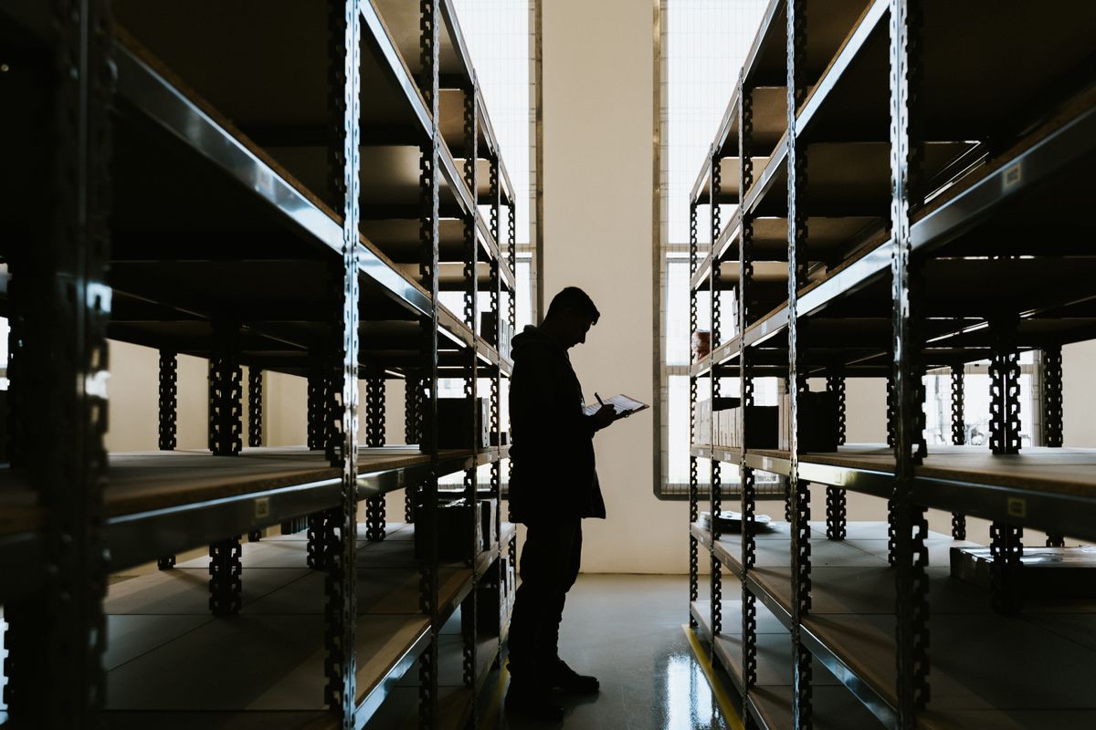 Warehouse staff member with a clipboard conducting an asset audit among storage racks
