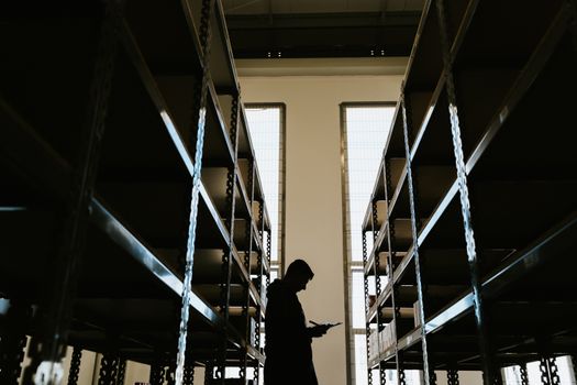 Backlit silhouette of a person holding a clipboard in a warehouse aisle in Curitiba, Brazil.