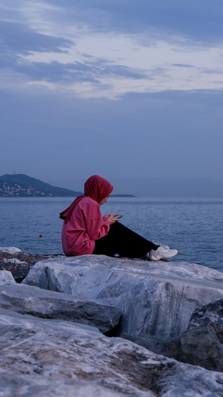 Woman In Red Hijab Sitting On Big Rock On The Bay