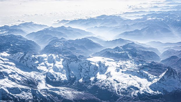 Breathtaking birds-eye view of a vast, snow-capped mountain range under a clear winter sky.