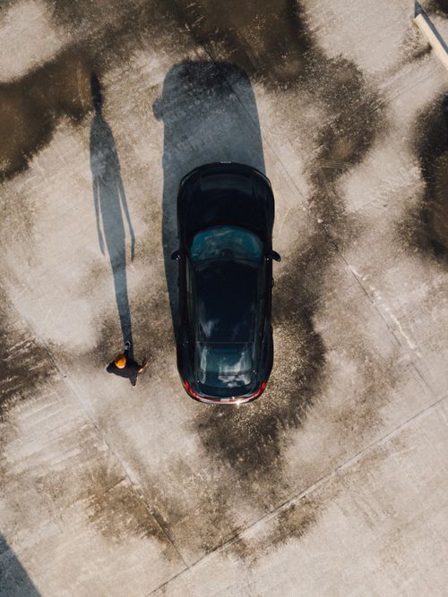 Free Drone captures a black car and a man walking on a concrete surface in Curitiba. Stock Photo