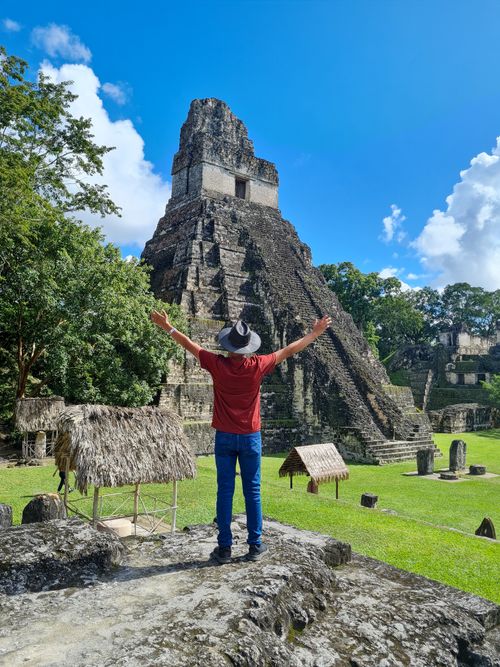 Free A person in a hat stands with arms raised viewing the Temple I at Tikal against a blue sky. Stock Photo