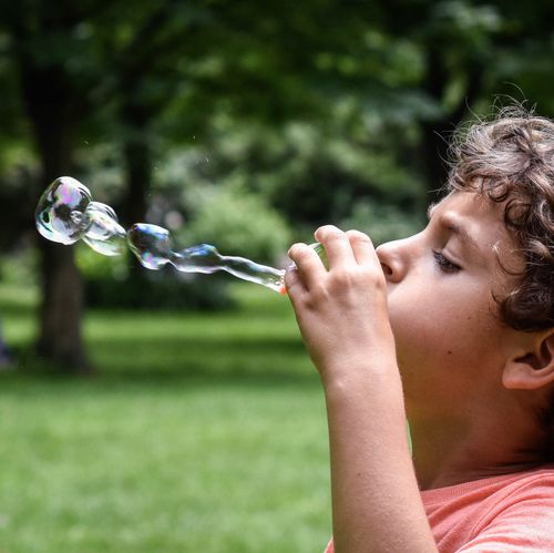 Free A young boy enjoys blowing bubbles in a green outdoor park setting during the day. Stock Photo