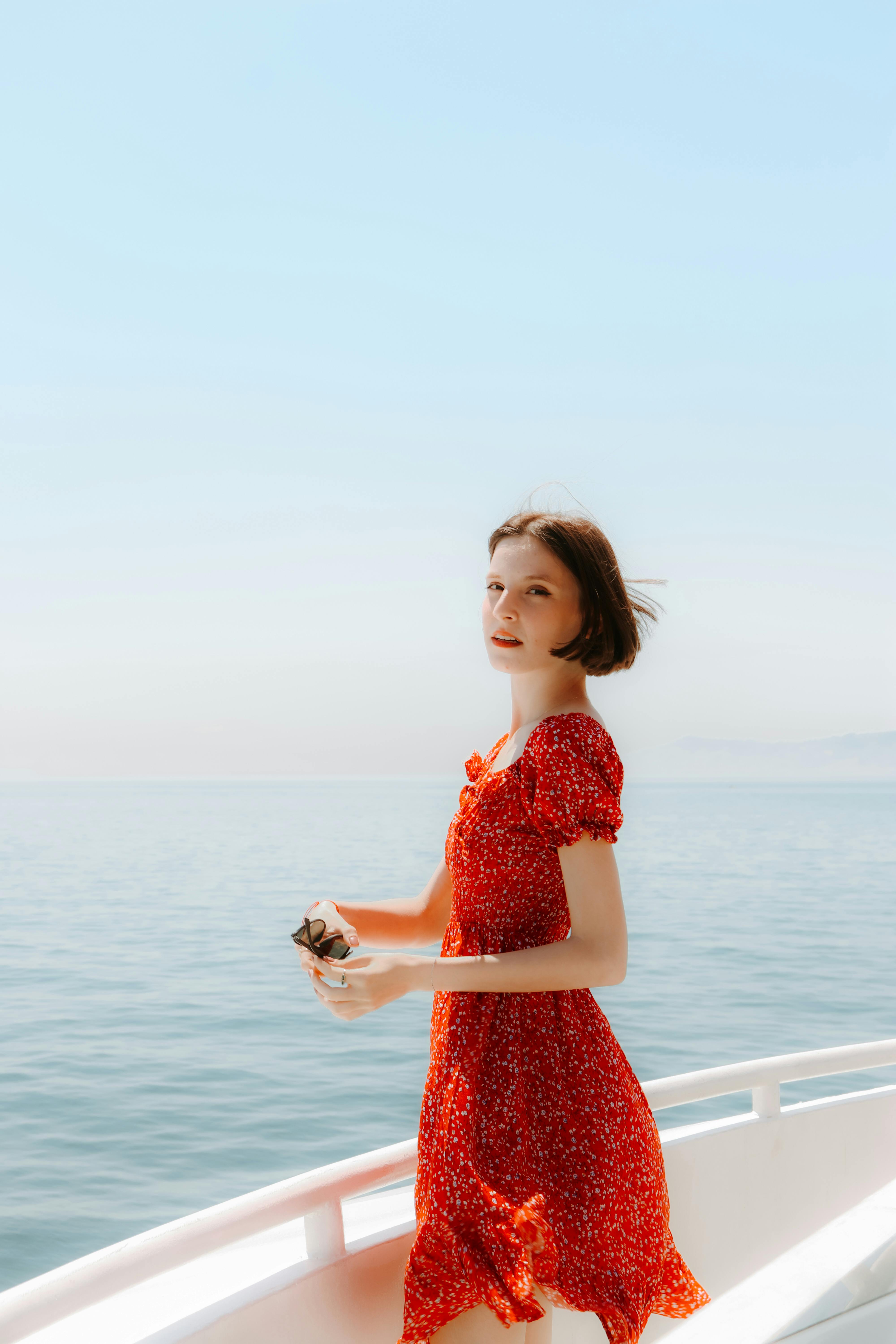 Woman in red dress enjoys a sunny day on a boat with a serene sea backdrop.