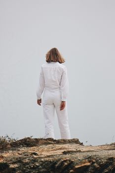 Woman in white suit standing on a cliff edge, symbolizing freedom and solitude.