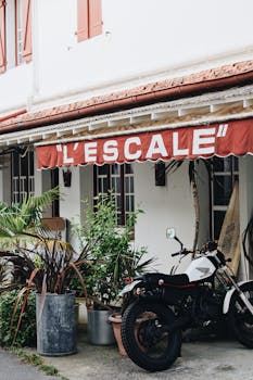 A vintage motorcycle parked outside L'Escale restaurant with lush plants and a charming storefront.