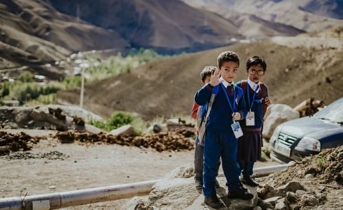 Free Group of children in school uniforms waving, set against a mountainous landscape. Stock Photo