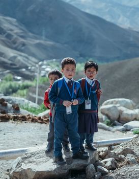 Three children in school uniforms standing together on a rocky path in a mountainous area.