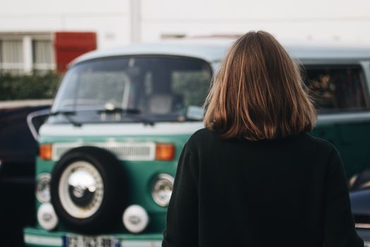 A woman with brunette hair stands facing a vintage van, captured with a bokeh effect.