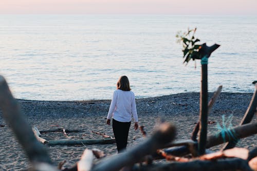 Woman in White Long Sleeve Shirt Standing on Beach Shore