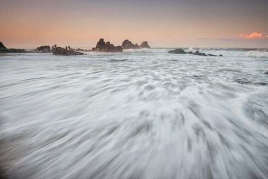 Serene long exposure shot of waves crashing against rocks at sunset, capturing motion and tranquility.