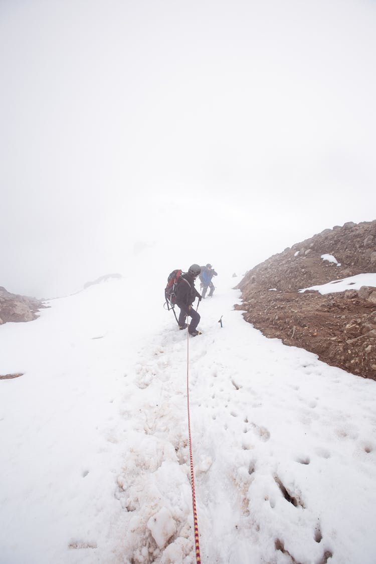 People Hiking On A Snow Covered Mountain While Holding On Rope