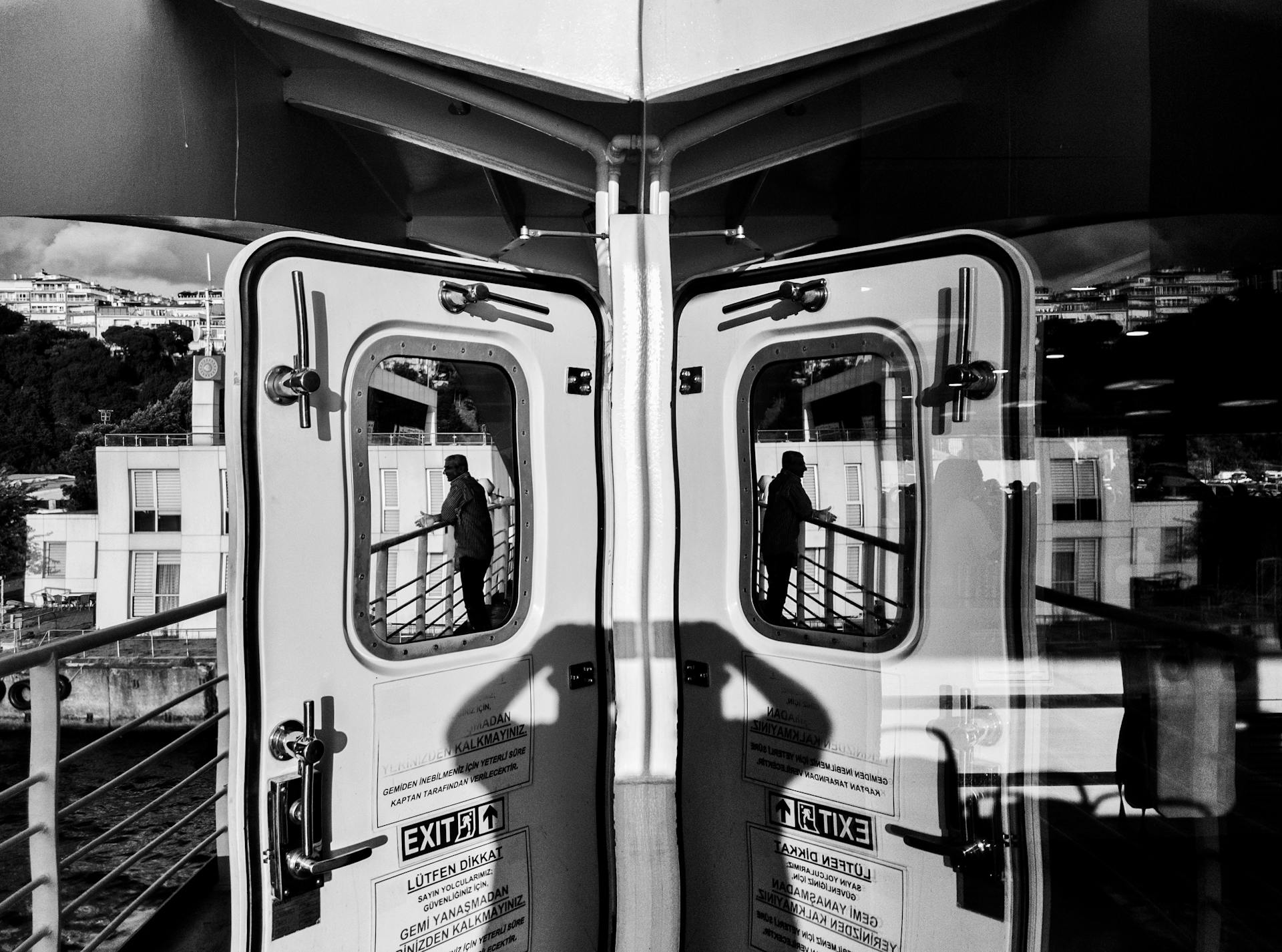 A reflective black and white image showing a man and exit doors on a ferry in İstanbul.