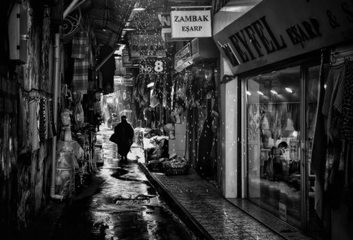 Black and white photo of a rainy alley in Istanbul's bustling market with people walking.