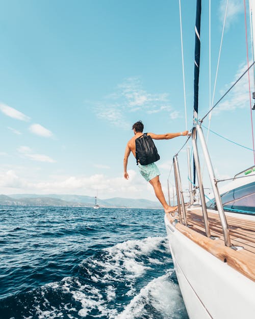 Free Man Wearing Backpack Standing On Side Of Boat During Daytime Stock Photo