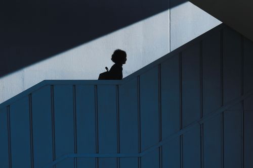 Free Minimalist silhouette of a person walking up a staircase, creating contrast in a shadowed architectural space. Stock Photo
