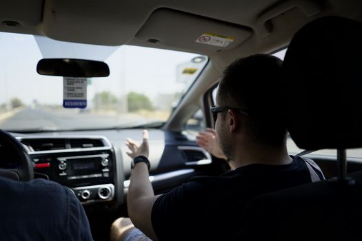 Passenger gesturing while conversing during a car journey on a sunny day.