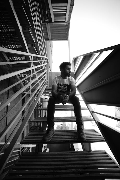 Free Grayscale Photo of Man in Crew Neck T-shirt and Pants Sitting on Stairs Stock Photo