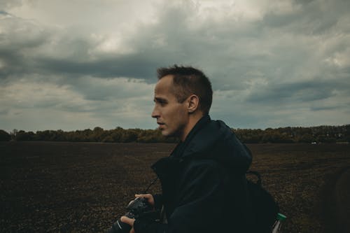 Man in Black Jacket Standing in a Field Holding Camera