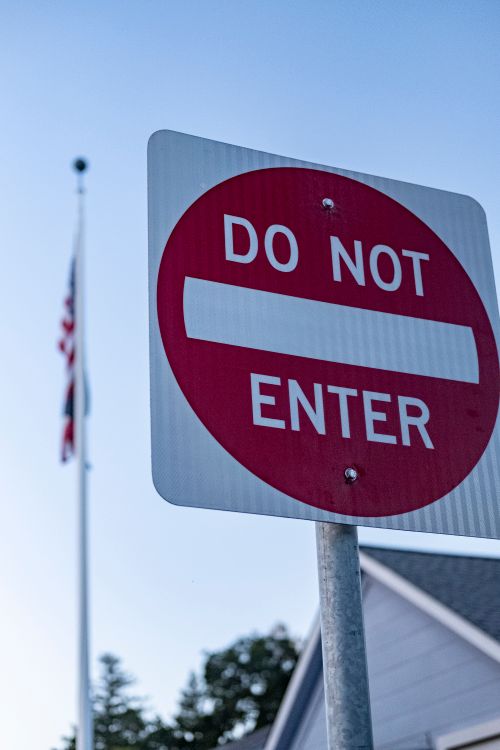 Free Close-up shot of a 'Do Not Enter' sign with a blurred American flag in the background. Stock Photo