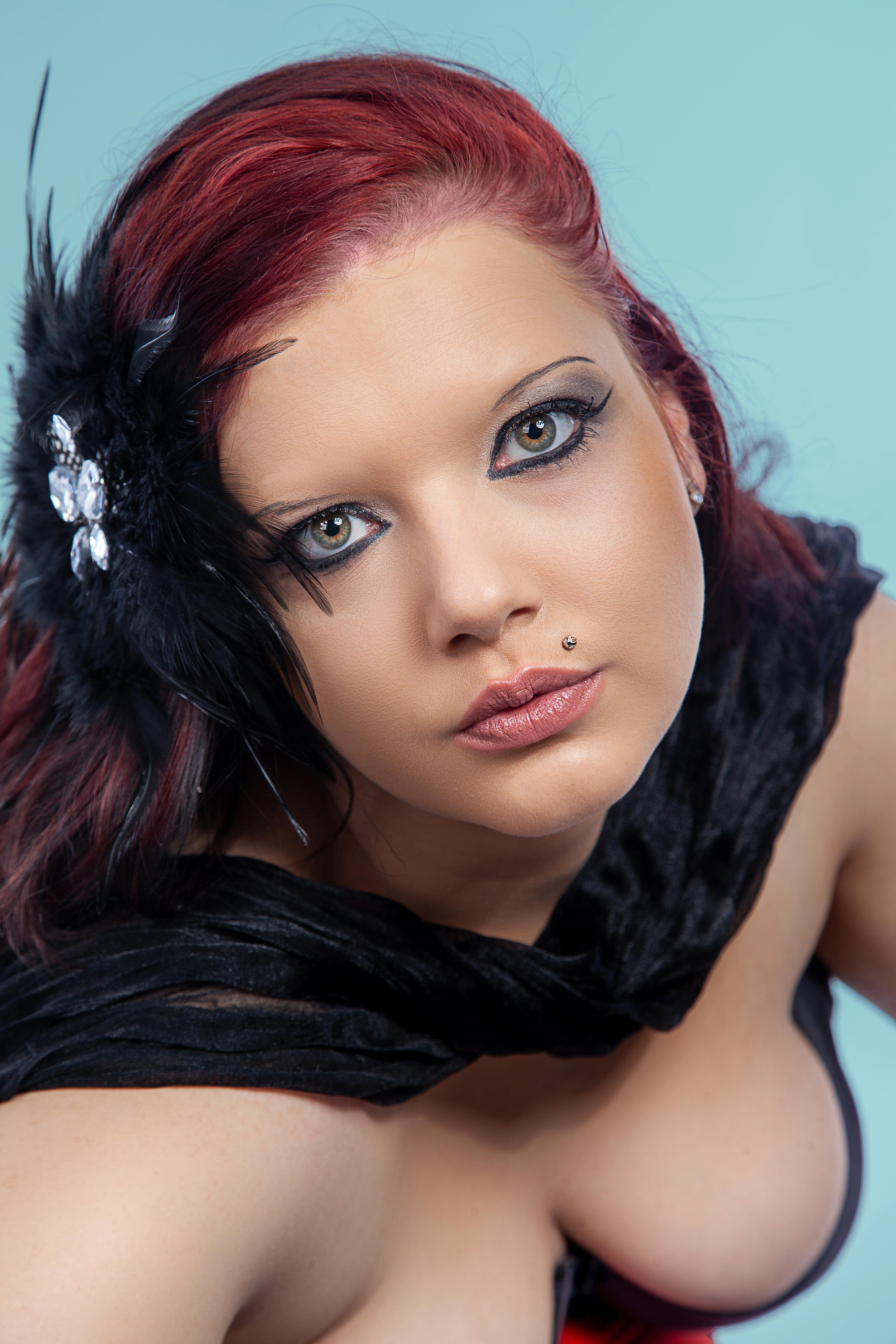 Close-up portrait of a woman with striking red hair and black feather accessory, showcasing eye makeup in Leipzig, Germany.