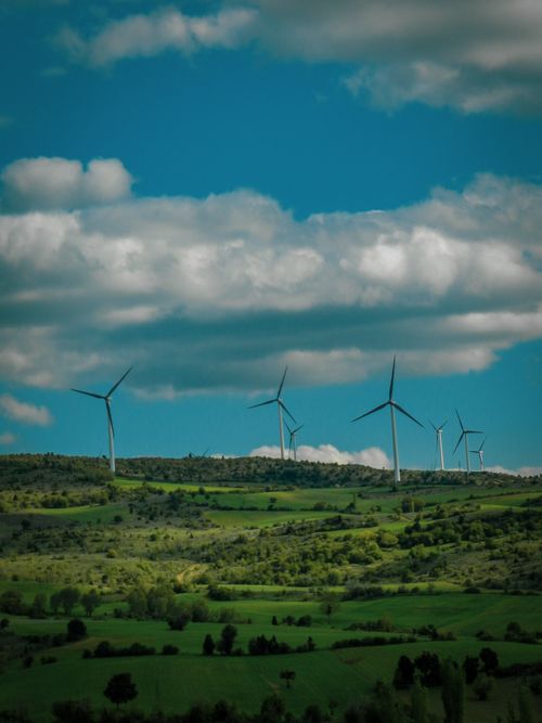 Free Scenic view of wind turbines on lush green hills with a bright blue sky and clouds. Stock Photo