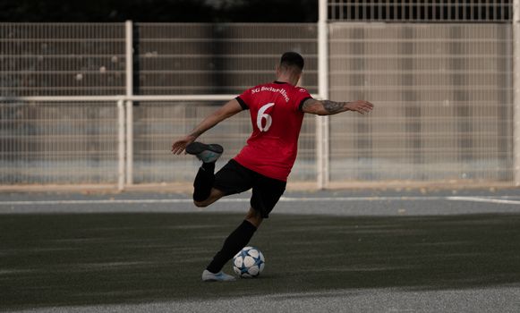 Male soccer player in red jersey kicks ball on an outdoor field during the day.