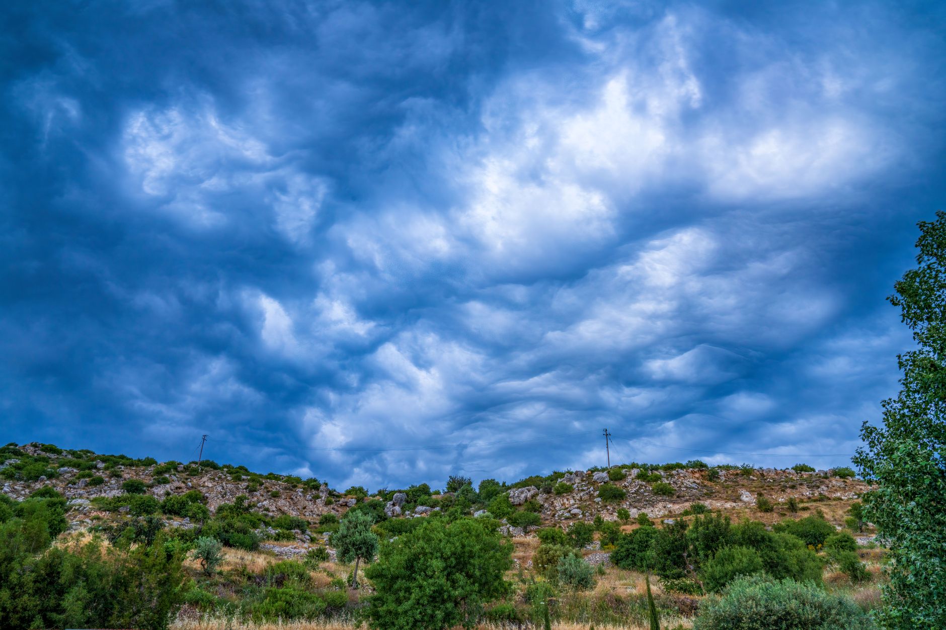 Vivid cloud formations gather above a rugged rural hillside, creating a scenic view.