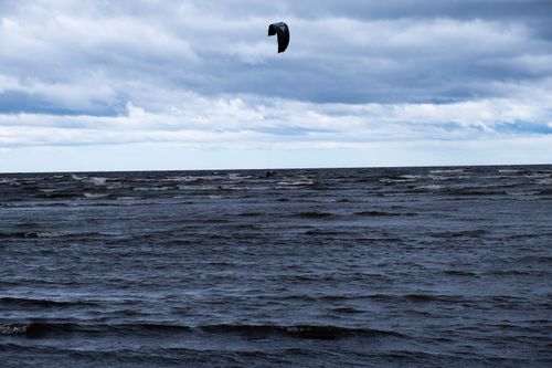 Free Vast ocean view with kite surfer beneath dramatic clouds. Perfect for travel and adventure themes. Stock Photo