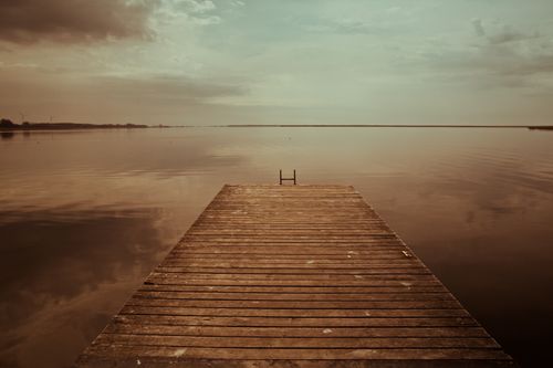 Free A peaceful view of a wooden jetty extending into a calm lake at sunset, with sepia tones. Stock Photo