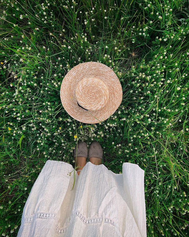 Top View Of Woman Feet Standing And Hat Lying On Grass 