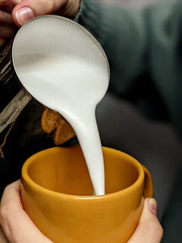 Close-up of frothed milk being poured into a yellow mug, creating a delicious coffee drink.